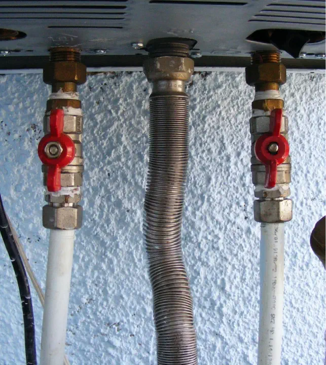 Close-up of four connected pipes with red valve handles beneath a metal panel, essential components in an HVAC system for efficient home heating.