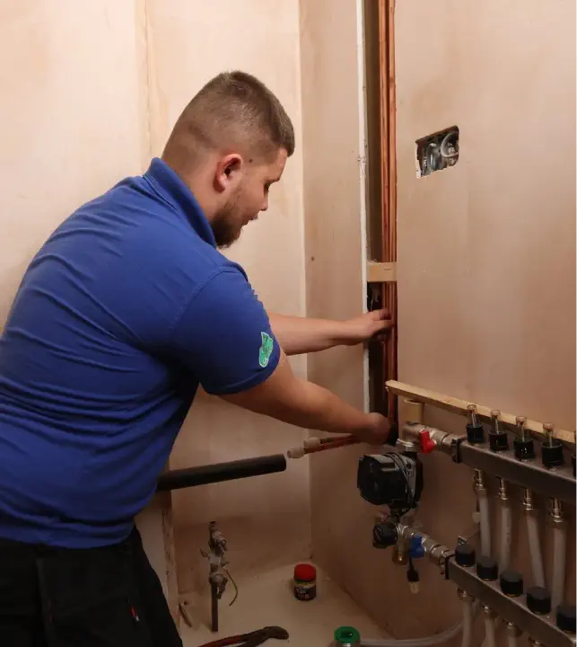 A JBL technician wearing a blue shirt is installing or repairing plumbing pipes and fittings on a wall, embodying the expertise.