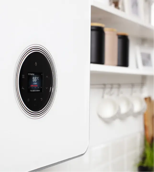 Close-up of a modern white heating unit displaying a temperature of 55°C, installed in a kitchen with white tiles and shelves holding jars and mugs, illustrates the efficiency of LPG boilers.